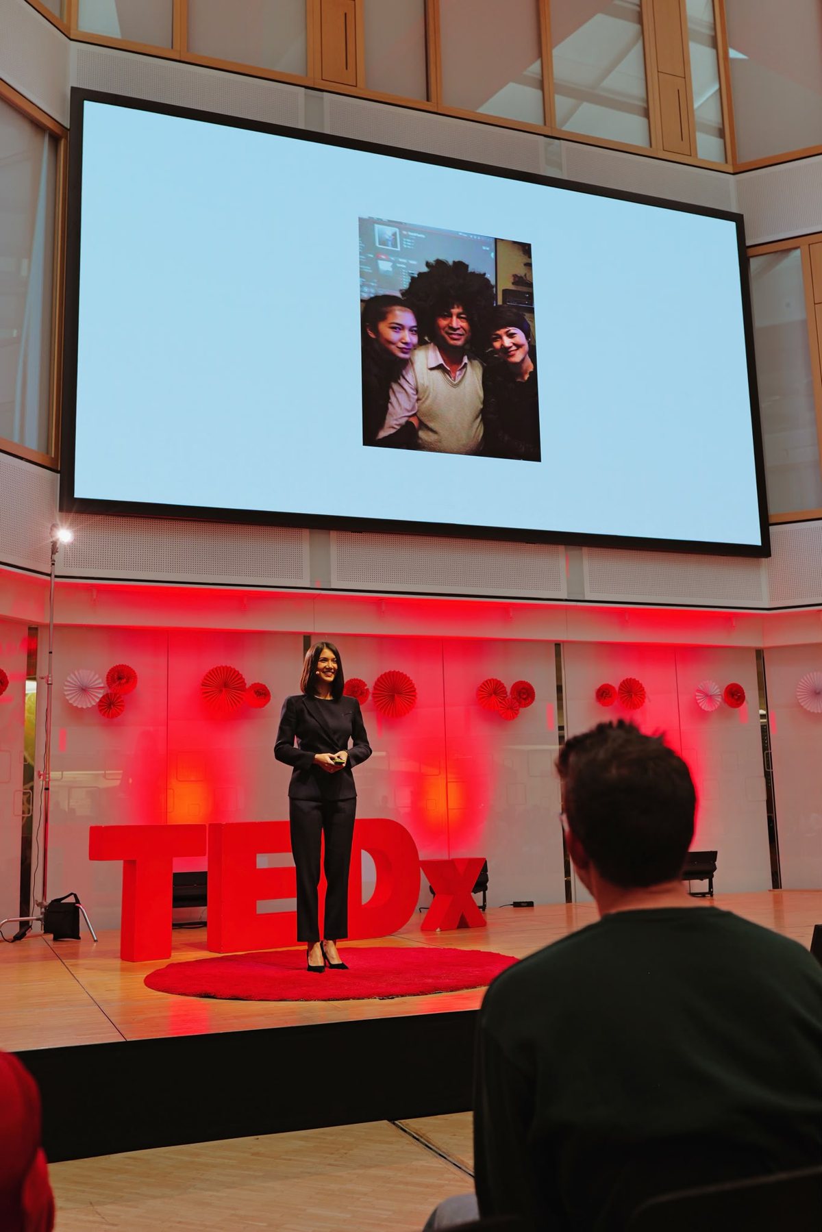 Ayimire Dilimulati on the TEDxKarlsruhe stage, with a family photo on the screen behind her